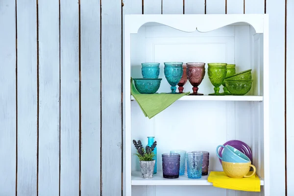 Clean glasses, plates and cutlery on shelves in kitchen cupboard — Stock Photo, Image