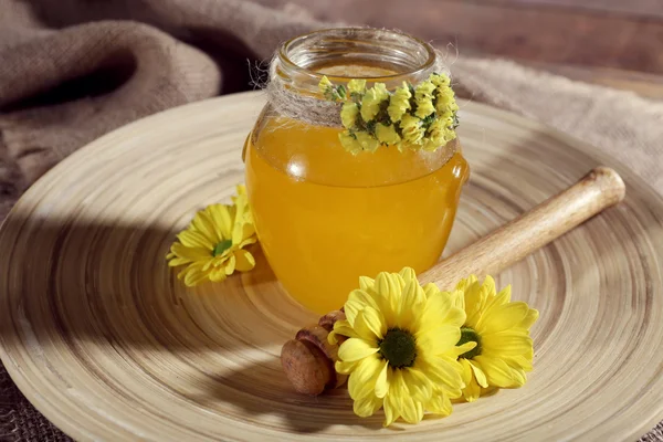 Tarro de miel con flores en bandeja de madera, primer plano — Foto de Stock