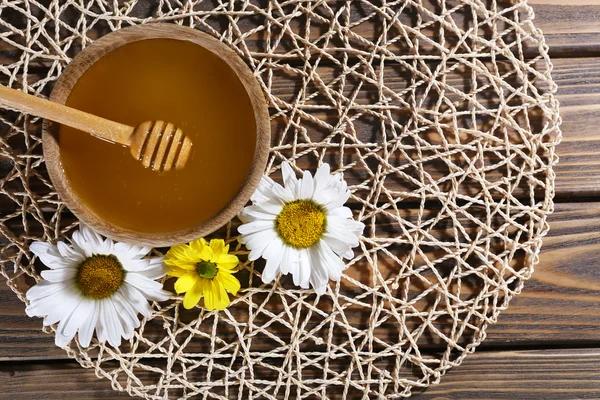 Μέλι σε κατσαρόλα και σε μπολ, ξύλινη κουτάλα και λουλούδια σε λυγαριά χαλί σε ξύλινα φόντο — Φωτογραφία Αρχείου
