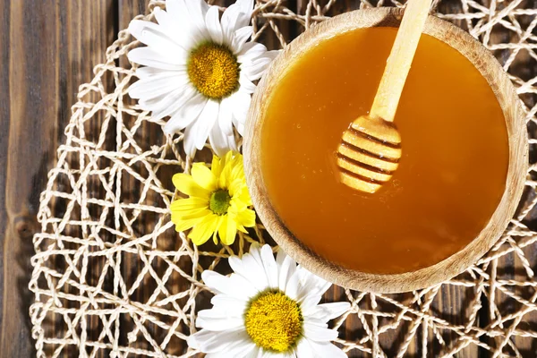 Miele in vaso e in ciotola, paletta di legno e fiori su tappetino di vimini su fondo di legno — Foto Stock