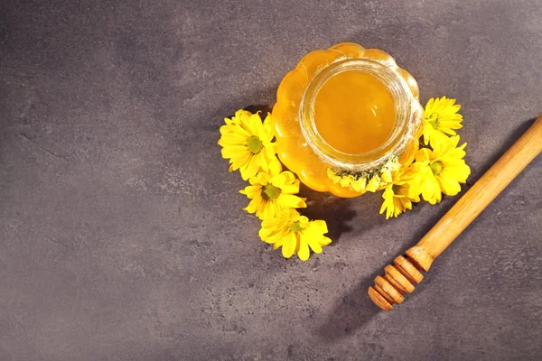 Pot of honey with wooden dipper and yellow flowers on grey background — Stock Photo, Image