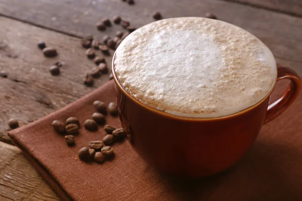 Taza de café en servilleta y granos de café sobre fondo de madera —  Fotos de Stock