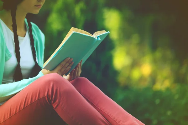 Young woman with book sitting on green grass outdoors — Stock Photo, Image