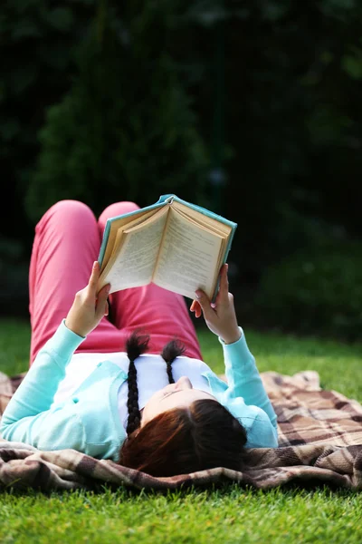 屋外の緑の草の上に横たわる本を持つ若い女性 — ストック写真