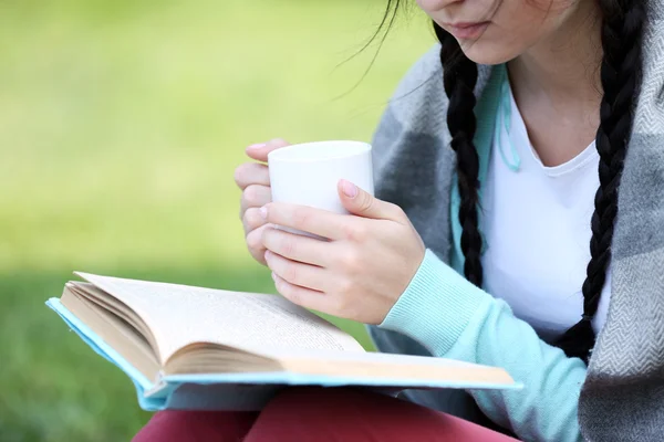 Mujer joven con libro sentado en la hierba verde al aire libre — Foto de Stock