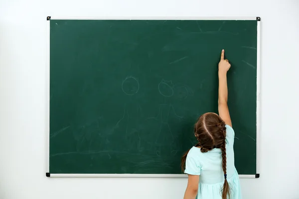 Menina apontando para algo no quadro negro na sala de aula — Fotografia de Stock