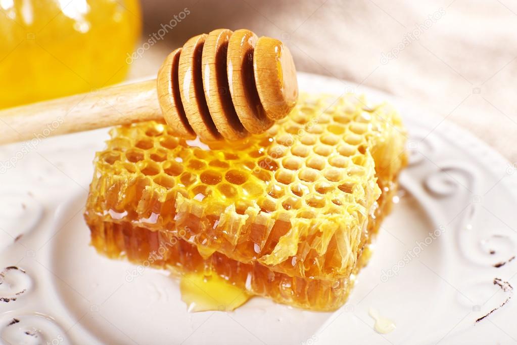 Honeycomb, dipper on white plate and pot of honey closeup