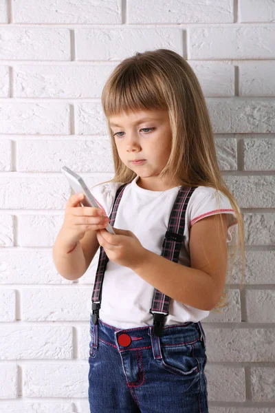 Vacker liten flicka med mobiltelefon på ljus vägg bakgrund — Stockfoto