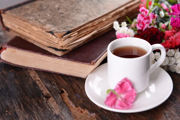 Old books with beautiful flowers and cup of tea on wooden table close up — Stock Photo, Image