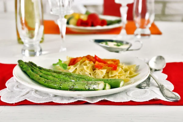Roasted asparagus and tasty pasta with vegetables on plate on wooden table background — Stock Photo, Image