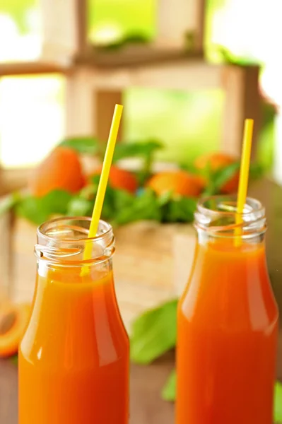 Bottles of apricot juice and fresh fruits on table close up — Stock Photo, Image