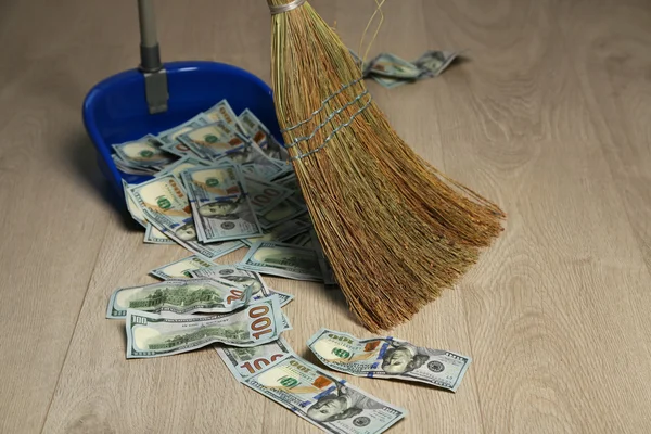 Метла выметает доллары в мусорном ведре на фоне деревянного пола — стоковое фото