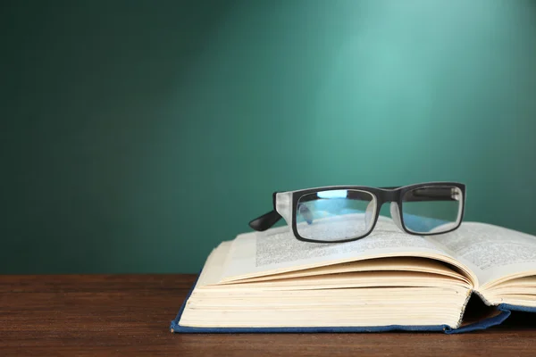 Otevřená kniha s brýlemi na stole na pozadí zelených tabuli — Stock fotografie
