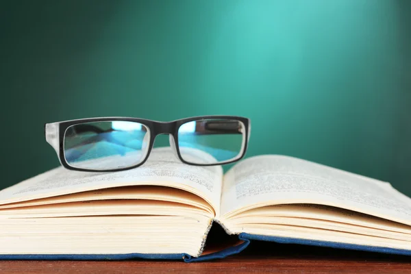Öppen bok med glasögon på skrivbord på gröna svarta tavlan bakgrund — Stockfoto