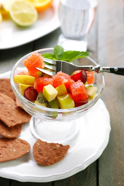 Insalata di frutta in una ciotola di vetro, su sfondo di legno — Foto Stock