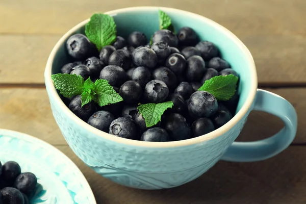 Cup and plate with fresh blueberries on wooden table close up — Stock Photo, Image
