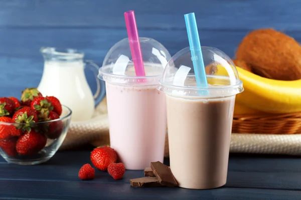 Plastic cups of milkshake on color wooden background — Stock Photo, Image