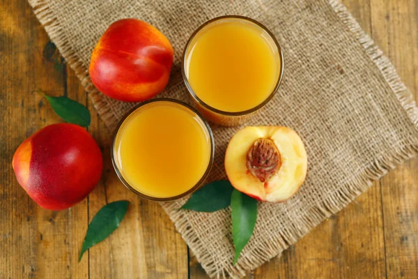 Спелые персики и стакан сока на деревянном фоне — стоковое фото