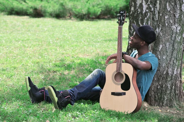 Man with guitar sitting in park — Stock Photo, Image