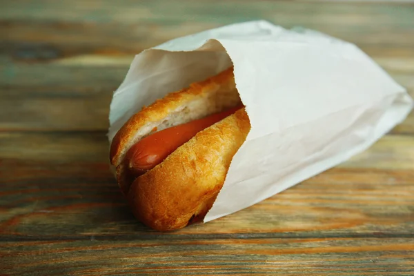 Čerstvý hot dog v papírový sáček na dřevěné pozadí — Stock fotografie