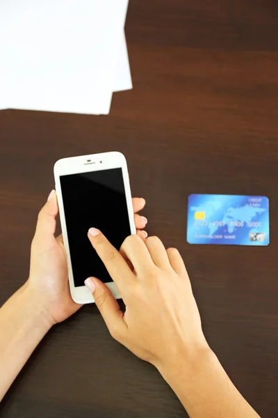 Mujer verifica saldo de cuenta en smartphone con aplicación de banca móvil sobre fondo de mesa de madera —  Fotos de Stock