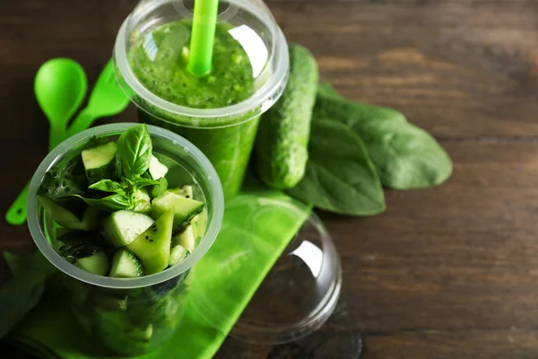 Ensalada de verduras y frutas verdes y bebida fresca saludable en tazas de plástico sobre fondo de madera. Colorido concepto de dieta — Foto de Stock