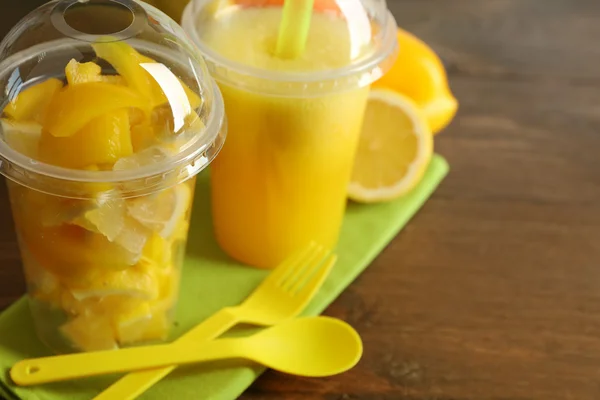 Gelber Gemüse- und Obstsalat und gesundes frisches Getränk in Plastikbechern auf Holzgrund. Buntes Ernährungskonzept — Stockfoto