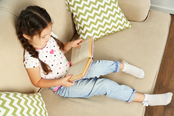 Menina sentada no sofá com livro — Fotografia de Stock