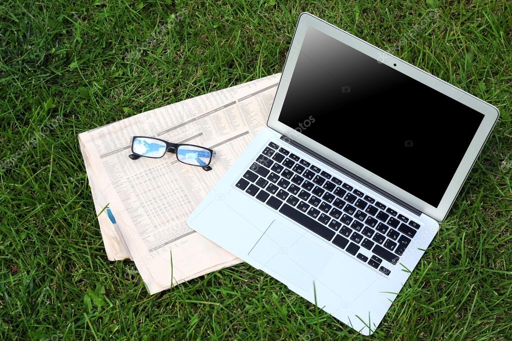 Laptop, newspaper and glasses on the green lawn