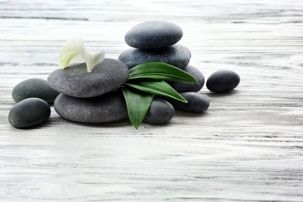 Piedras de spa con flores y hojas verdes sobre fondo de madera — Foto de Stock