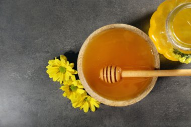 Kavanoz ve kase, ahşap kepçe ve çiçekler koyu gri arka plan üzerinde tatlım