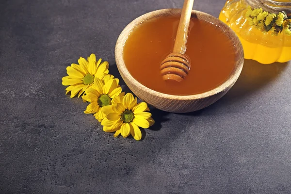 Honung i burk och i skål, trä dipper och blommor på mörk grå bakgrund — Stockfoto