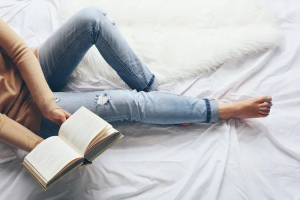 Frau in blauen Jeans liest Buch auf dem Bett — Stockfoto