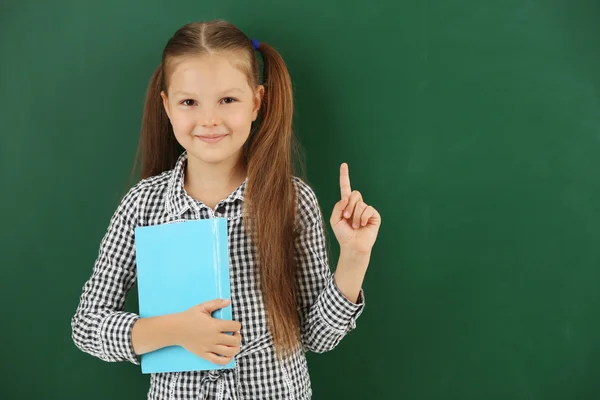 Beautiful little girl with book,  on blackboard background — Stock Photo, Image