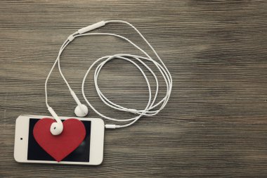 Hareket eden telefon ve kulaklık ile ahşap arka plan üzerinde kırmızı kalp