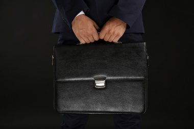 Koyu arka plan üzerinde evrak çantası ile takım elbiseli şık adam