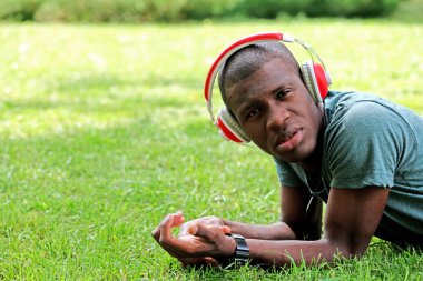 Afro-Amerikan yakışıklı kulaklıklarla yeşil çim üzerinde yalan