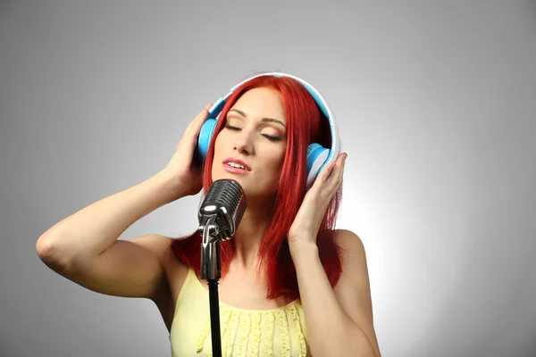 Hermosa mujer joven con micrófono y auriculares sobre fondo gris —  Fotos de Stock