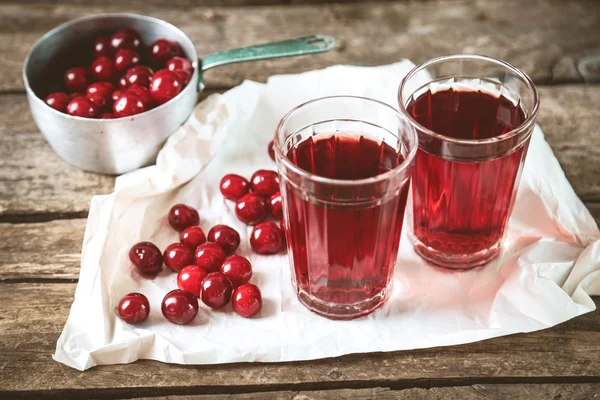 Dvě skleničky s cherry šťáva na stole, na dřevěné pozadí — Stock fotografie