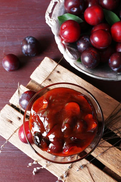 Tasty homemade plum jam in glass saucer on wooden board, closeup — Stock Photo, Image
