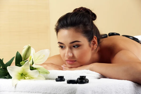 Mujer joven con piedras de spa en la espalda en la mesa de masaje en el salón de spa de belleza —  Fotos de Stock