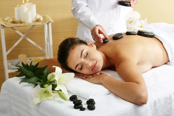 Mujer joven con piedras de spa en la espalda en la mesa de masaje en el salón de spa de belleza —  Fotos de Stock