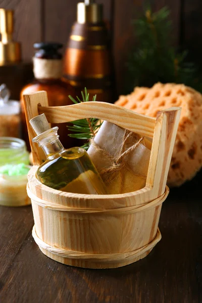 Essential oil of pine, handmade soap in wooden bucket and spa treatments on wooden background — Stock Photo, Image