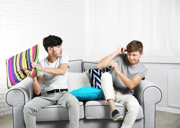 Dos hermanos peleando con almohadas en el sofá en casa —  Fotos de Stock