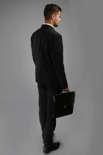 Elegant man in suit with briefcase on gray background — Stock Photo, Image