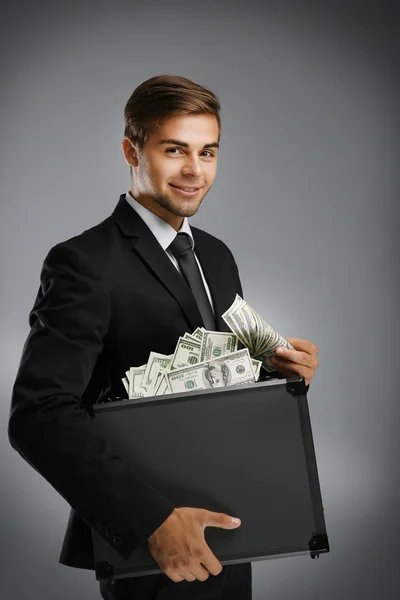 Homem elegante segurando caso com dinheiro em fundo cinza — Fotografia de Stock