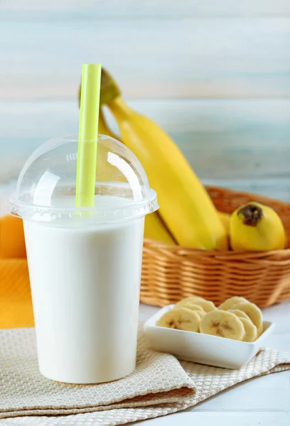 Plastic cup of milkshake with banana on color wooden background — Stock Photo, Image