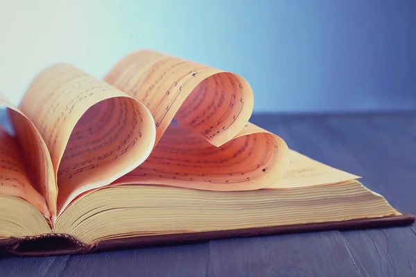 Book pages curved into hearts shapes on blue background — Stock Photo, Image