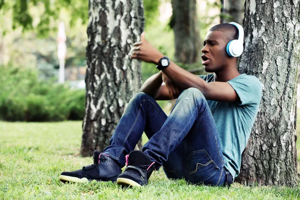 Bonito afro-americano com fones de ouvido sentado no parque — Fotografia de Stock