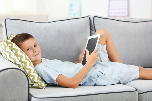 Menino com tablet digital sentado no sofá, em casa fundo interior — Fotografia de Stock